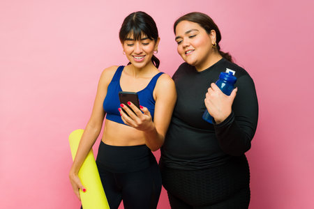Fit happy women friends texting on the smartphone or using a fitness app after an active workout