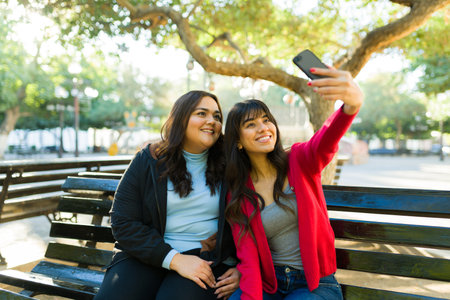 Attractive women friends taking a selfie with the smartphone for social media at the bench park