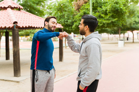 Active men friends doing a fist bump and happy about exercising or going on a run together outdoorsの写真素材