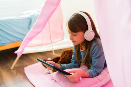 Cute little girl using a tablet with headphones while playing videogames or watching online videos