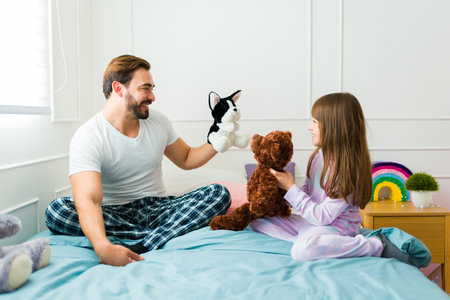Cheerful smiling father in pajamas playing puppets with her cute daughter after waking up in bedの写真素材