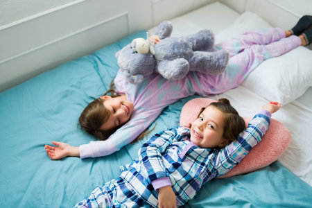 Cute caucasian girl having a fun sleepover with her best friend while resting in bed during the...