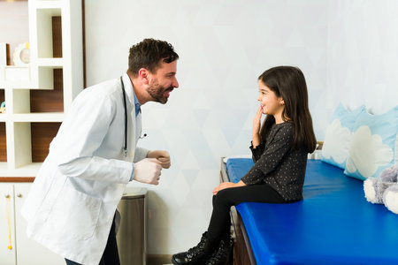 Profile of a happy caucasian pediatrician smiling to a cheerful adorable young kid coming for a...