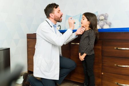 Pediatrician treating a little girl sick with asthma explaining how to an inhaler for an asthma...