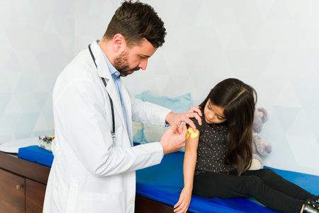 Caucasian pediatrician doctor putting an injection vaccine or sensory device to a sick young childの写真素材