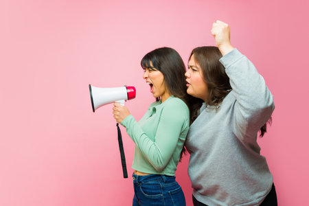 Angry latin young women looking upset while participating in a protest screaming with a megaphoneの写真素材