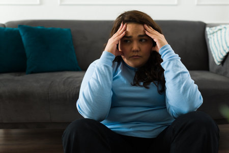 Depressed hispanic woman suffering from anxiety and depression feeling sad and crying alone at homeの写真素材