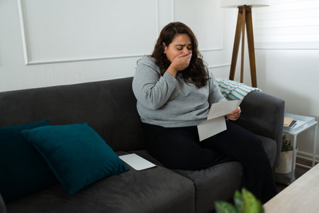 Surprised scared woman looking sad and shocked covering her mouth to scream after receiving a letter with bad newsの写真素材