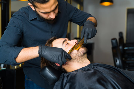 Side view of a caucasian man relaxing while getting a trim or shaving his beard at the barber shopの写真素材
