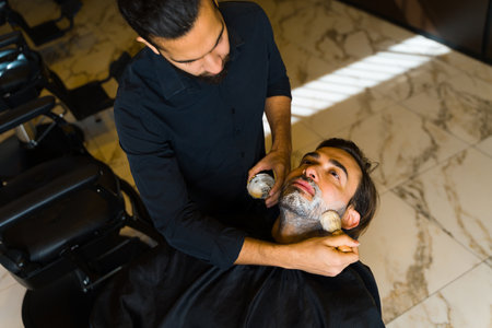 Top view of a caucasian man getting ready for grooming services while shaving his beard with a barberの写真素材
