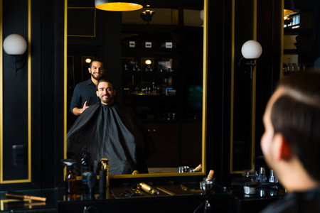 Cheerful male hairstylist and young man smiling looking in the mirror after getting a new trendy haircut at the salonの写真素材