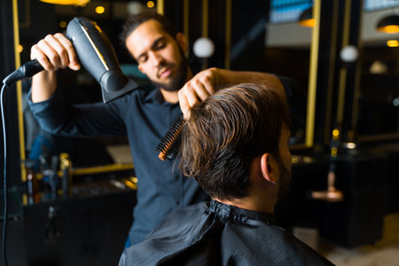 Close up of a male hairstylist using a blow dryer and a brush after cutting the hair of a man customer at the salonの写真素材