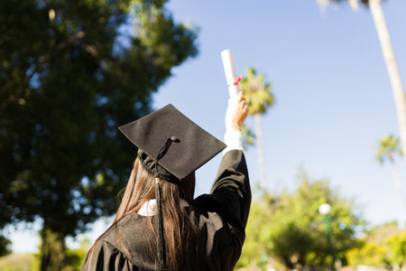 Rear view of a young woman graduate seen from behind with her graduation gown showing her university...