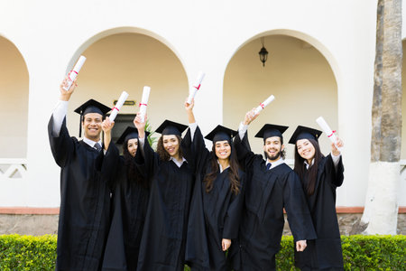 Attractive young women and men receiving their university diploma at graduation and celebrating