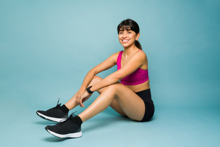 Happy hispanic woman in activewear making eye contact and smiling while looking ready to start her run or workout exercisesの写真素材