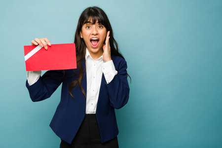 Excited beautiful woman wearing a professional suit looking surprised and happy about receiving good news from work in a letter messageの写真素材