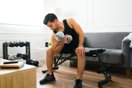Fitness young man doing bicep curls lifting dumbbell weights while working out at his home gymの写真素材