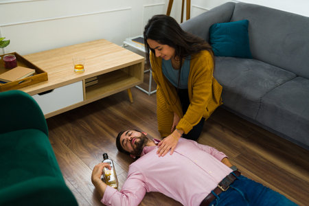 Scared young woman trying to help her passed out drunk husband in the living room after drinking...