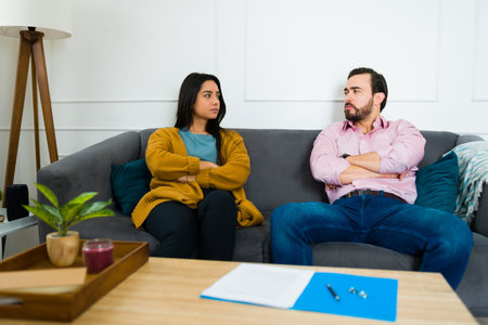 Angry young woman and man looking upset with their arms crossed sitting on the couch thinking about signing the divorce papersの写真素材