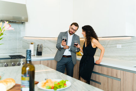 Handsome caucasian man and hispanic woman talking having a romantic time drinking wine at a luxury kitchen during a dateの写真素材