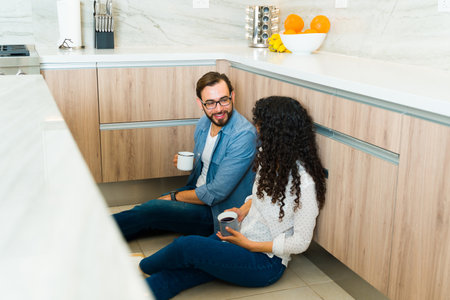 Relaxed happy woman and man sitting and relaxing in their big beautiful kitchen while drinking a cup of coffeeの写真素材