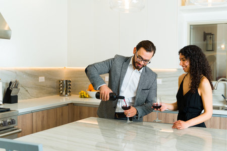 Attractive woman and caucasian man in a beautiful luxury kitchen opening a bottle of wine during an elegant dateの写真素材