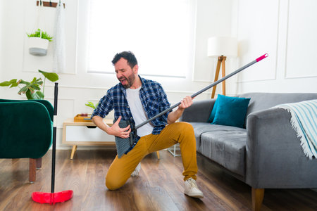 Excited caucasian man having fun while listening to music while sweeping and cleaning the living roomの写真素材
