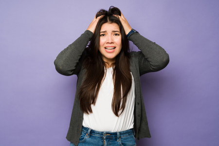 Stressed worried woman against a purple background holding her head and looking anxious because of her problemsの写真素材