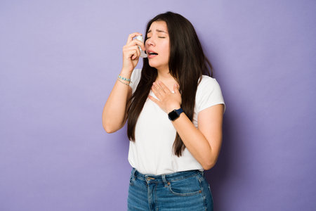Asthmatic sick young woman using an inhaler while having an asthma attack or with breathing problemsの写真素材