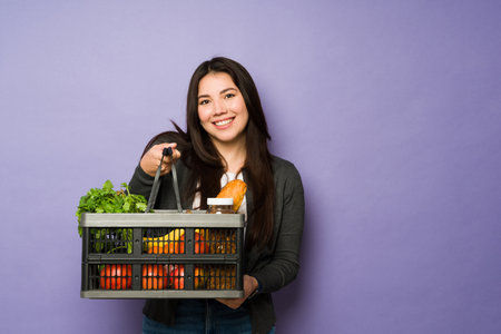 Beautiful asian woman in her 30s smiling while going grocery shopping and buying fruits and vegetables in a basketの写真素材