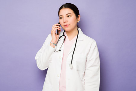 Caucasian woman doctor using a white coat and a stethoscope talking on the phone with a patientの写真素材