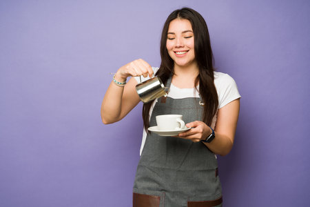 Happy female caucasian barista smiling while serving a coffee cup in front of a studio purple backgroundの写真素材