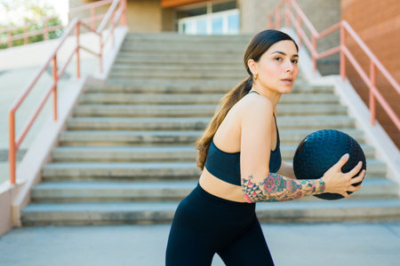 Gorgeous young woman in activewear exercising doing a cross training workout outdoors and using a slam ballの写真素材