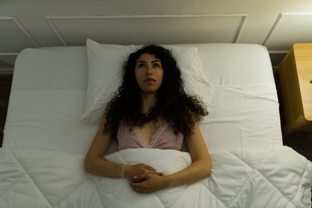Stressed young latin woman with a sleeping disorder suffering from insomnia while trying to sleep late at night in her bedroomの写真素材