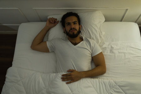 Upset hispanic young man lying awake at night while lying trying to sleep while suffering from...