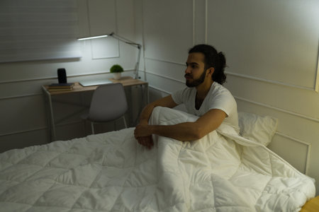 Angry latin man with curly hair sitting in bed waking up in the middle of the night while suffering from insomniaの写真素材