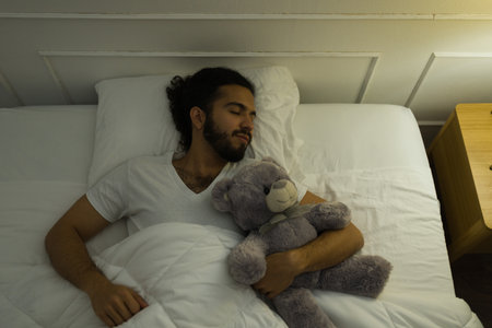Attractive happy man hugging his teddy bear and sleeping looking relaxed in a comfy bedの写真素材