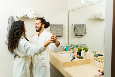 Romantic beautiful couple dancing with music in the bathroom while relaxing together in white robesの写真素材