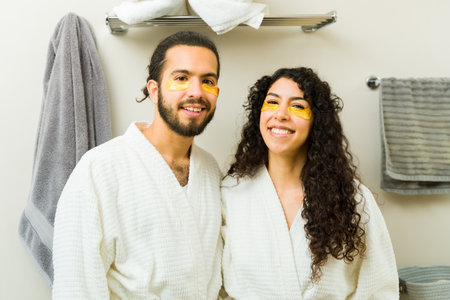 Attractive smiling couple making eye contact while relaxing in white robes after using grooming beauty products in the bathroomの写真素材