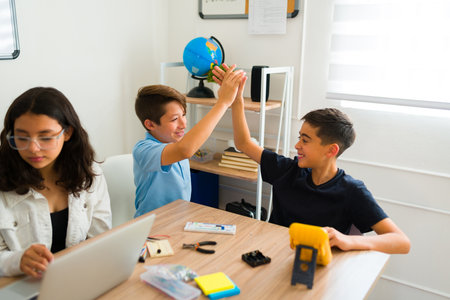 Excited teen young boys having fun doing a high five after doing a successful robot prototype...