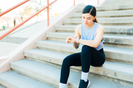 Happy beautiful woman in sportswear using her smartwatch and fitness app to start her running...