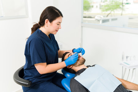Female dentist in blue scrubs smiling while doing a dental examination on a young man and checking for cavitiesの写真素材