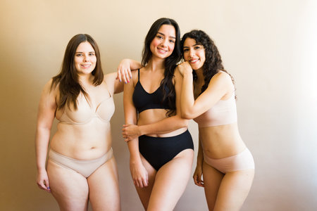Diverse young women in underwear looking feminine and happy while promoting body acceptance against a studio backgroundの写真素材