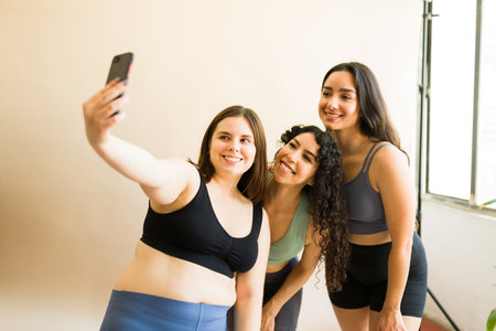 Attractive diverse women friends taking a selfie after finishing their active workout and...