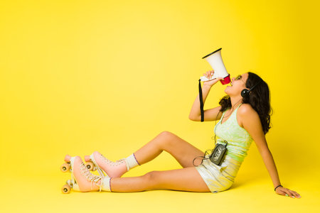 Side view of a cheerful teen girl screaming with a megaphone looking happy in vintage roller skates...