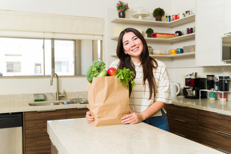 Attractive happy woman with a vegetarian lifestyle in the kitchen ready to cook healthy food with vegetables after going to the supermarketの写真素材
