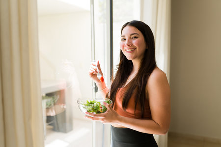 Happy vegetarian woman smiling while making eye contact and eating a healthy fit green saladの写真素材