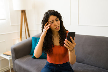 Stressed young woman suffering from eye strain or irritated eyes while texting and using her smartphoneの写真素材