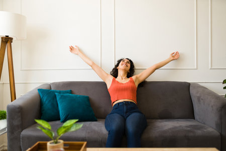 Attractive relaxed young woman feeling carefree and excited while relaxing sitting on the couch in the living roomの写真素材