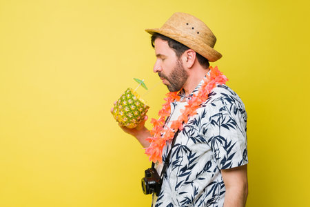 Profile of a relaxed man drinking a pineapple drink at the beach during his summer vacations in front of a yellow backgroundの写真素材